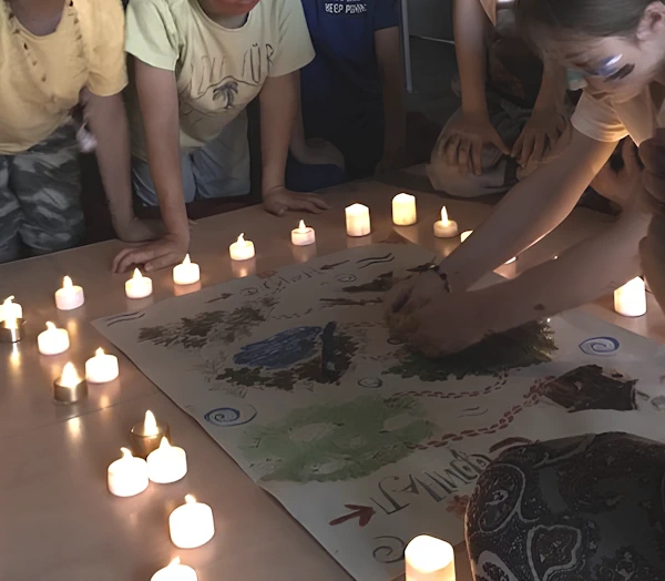 Группа детей играет в настольную игру в Чемодане Сказок. На столе зажжены свечи. Дети с интересом наблюдают за девочкой, которая делает ход.