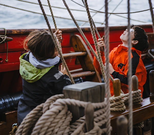Мальчик и ещё один ребёнок на корабле натягивают парусный канат.